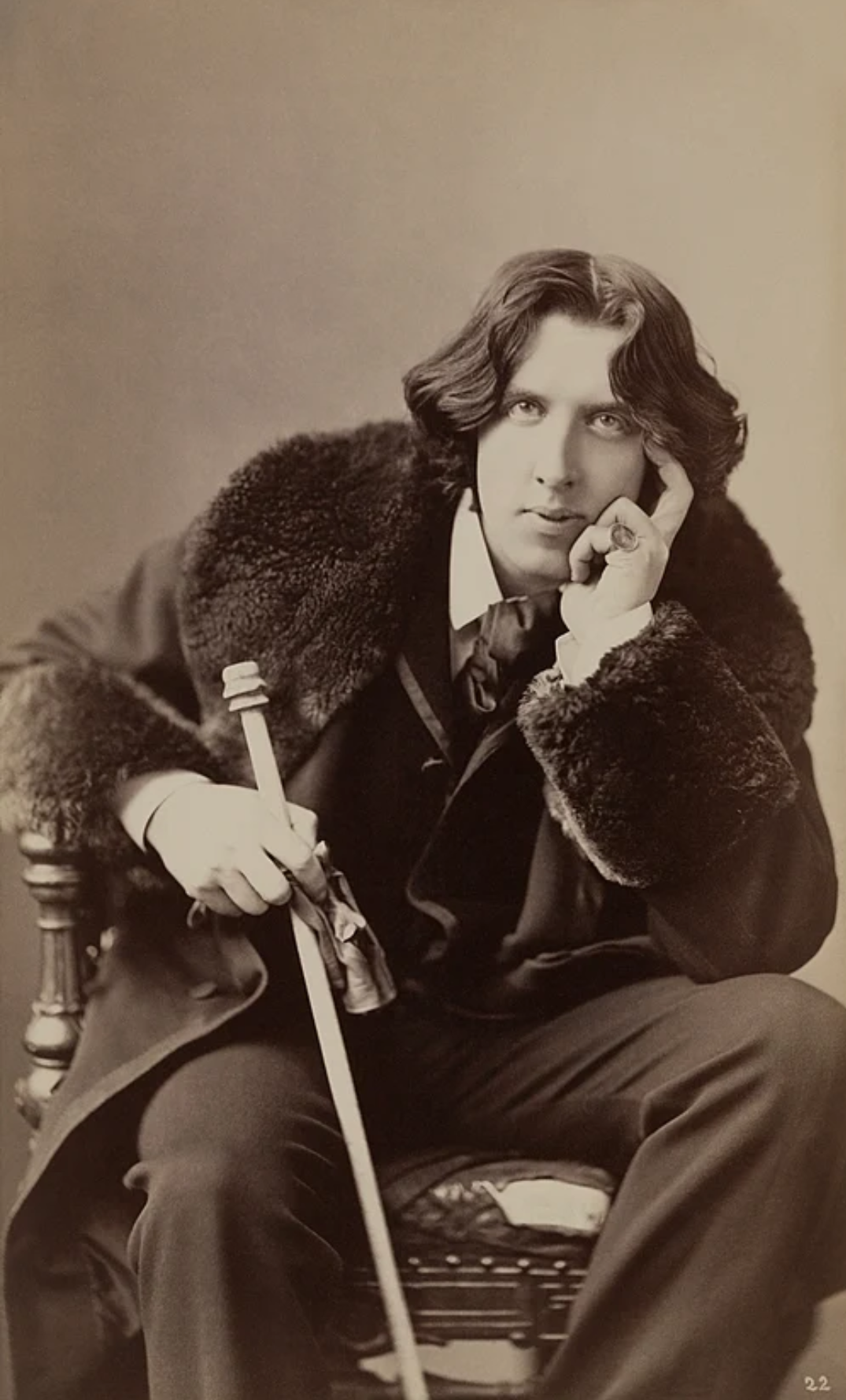 Oscar Wilde photographed by Napoleon Sarony in 1882, wearing a fur-trimmed coat and holding a cane